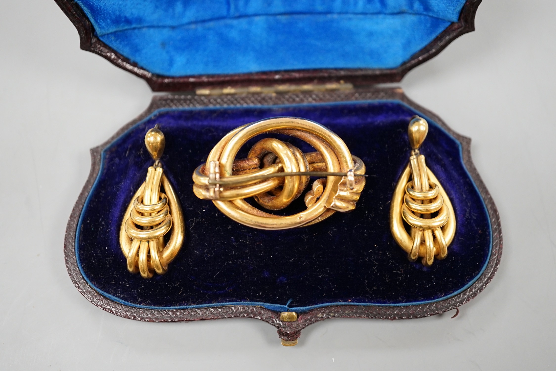 A cased Victorian yellow metal demi parure, comprising a brooch and pair of earrings of entwined knot form brooch width 43mm, gross weight 16.4 grams.